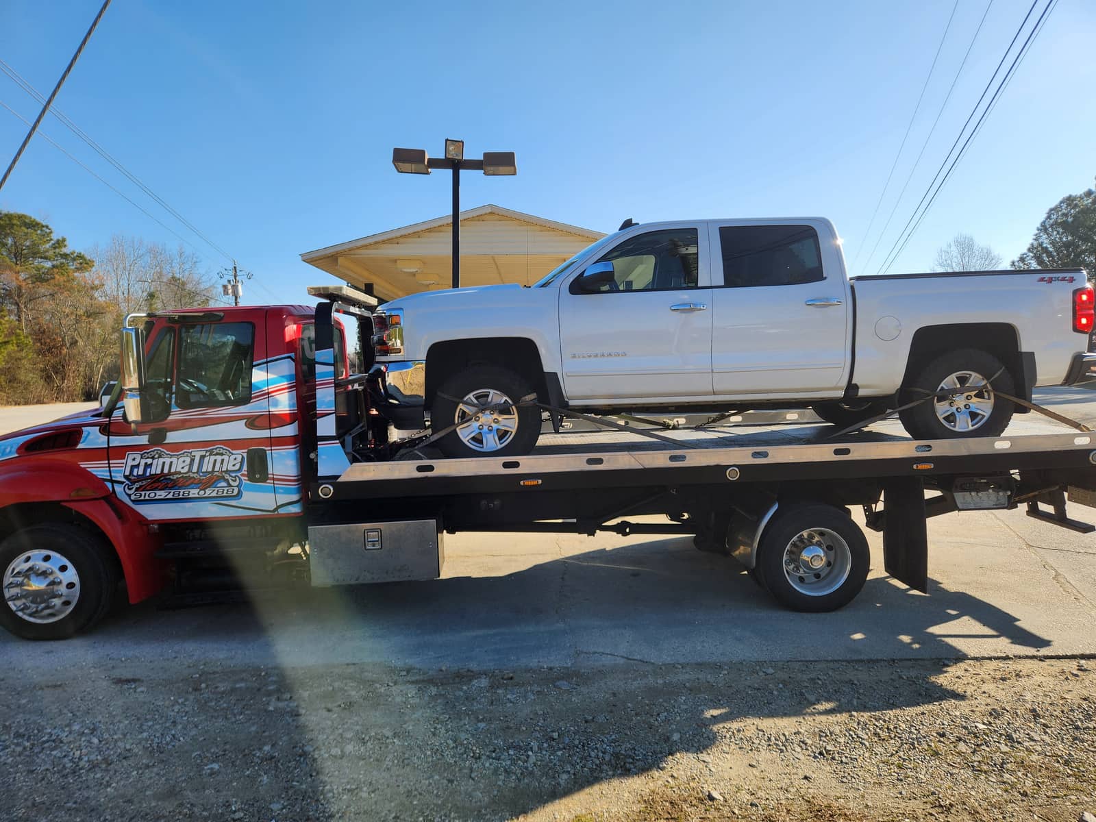 White Chevrolet Silverado 4x4 pickup truck chained down on the Prime Time Towing flatbed